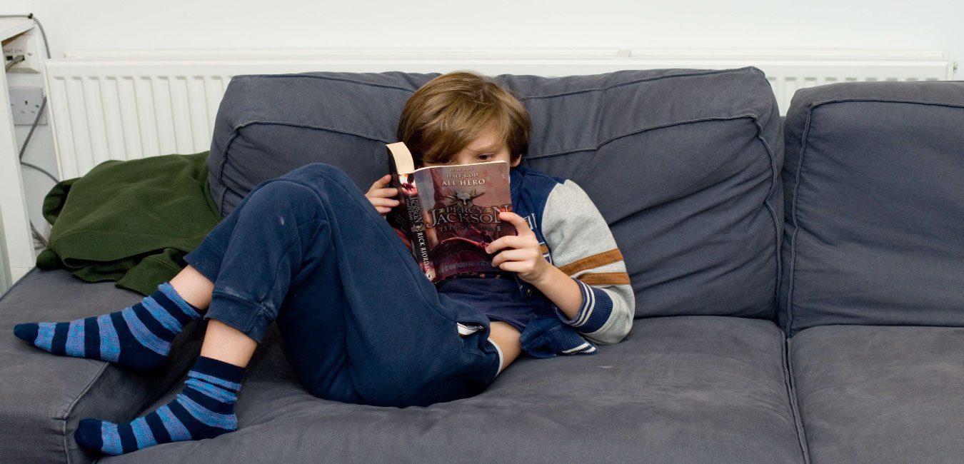 A young person from the Ministry of Stories enjoys reading a book curled up on the sofa