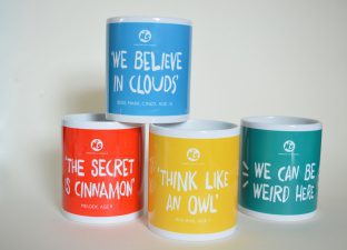 Four mugs in bright colours, featuring the four quotes "we can be weird here", "we believe in clouds", "the secret is cinnamon" and "think like an owl"