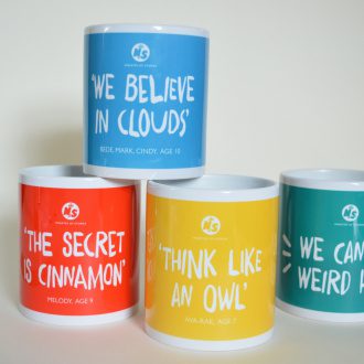 Four mugs in bright colours, featuring the four quotes "we can be weird here", "we believe in clouds", "the secret is cinnamon" and "think like an owl"