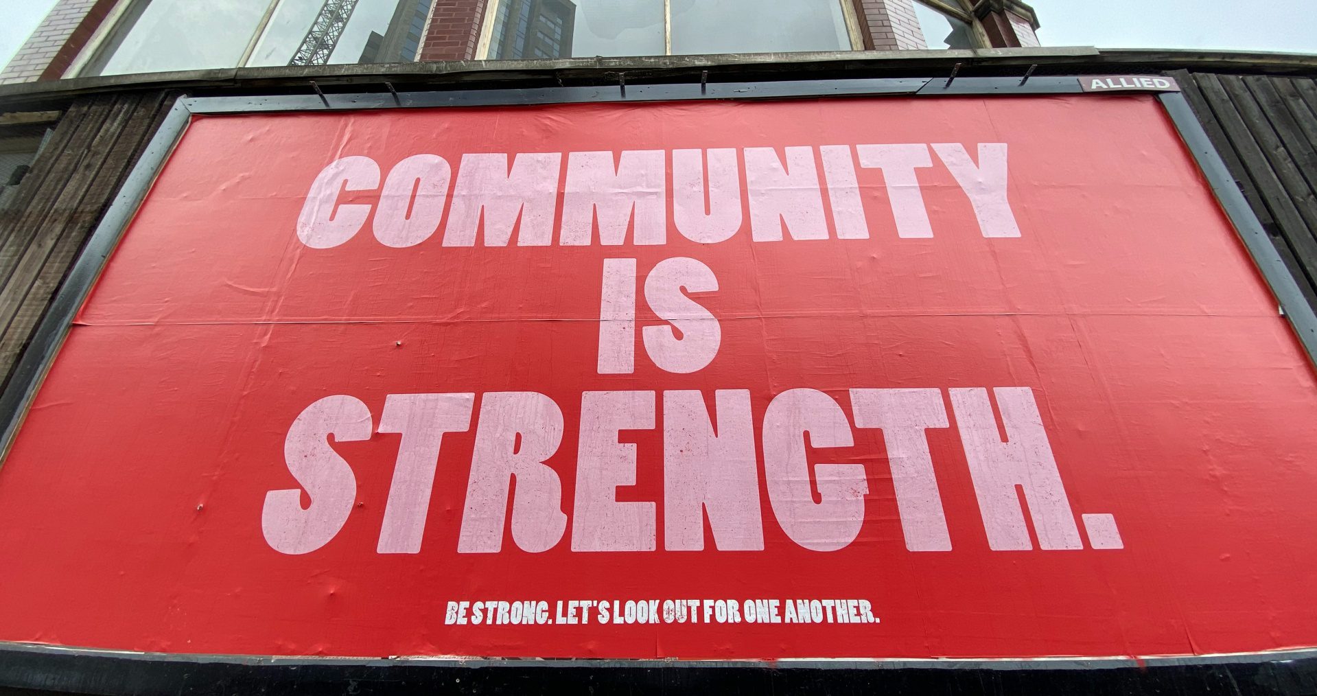 A large billboard with red and pink text proclaims 'community is strength' on Seven Sisters Road, London, UK