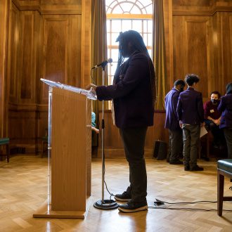 Young person stands silhouetted at a podium ready to give a speech they have written