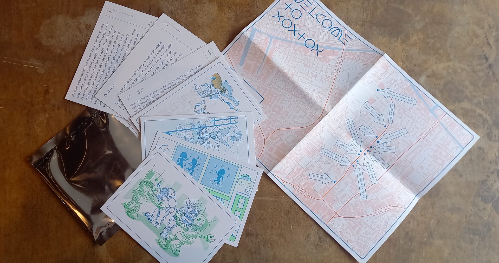 A pack of white postcards with bright, repo graphics is laid next to a map of a similar design on a wooden table