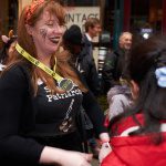 A adult fundraiser with red hair and a spider painted on her face smiles talking to a child just out of shot