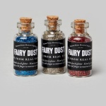 Three bottles of multicoloured glitter sits in tiny, corked glass bottles with a black label that reads Fairy Dust
