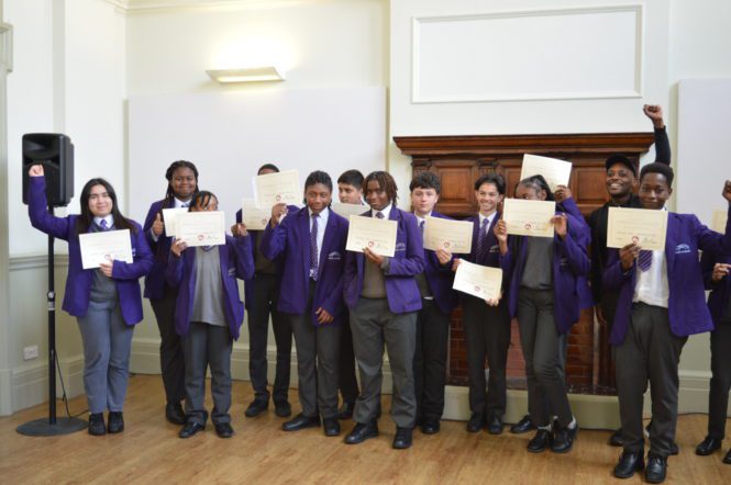 A group of young teenagers stand in a group proudly showing their certificates to the camera
