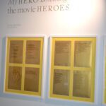 A bright, white wall displays writing on small pieces of white paper, framed against gold paper. There are two frames, each with four piece of writing displayed.