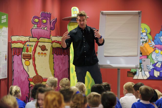Image of artist Aaron Blecha, running a drawing workshop in front of a room full of children.