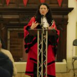 The Speaker of Hackney is Councillor, Anya Sizer, stands at the lexturn, in red ceremonial robes. She address the room with animated hands.