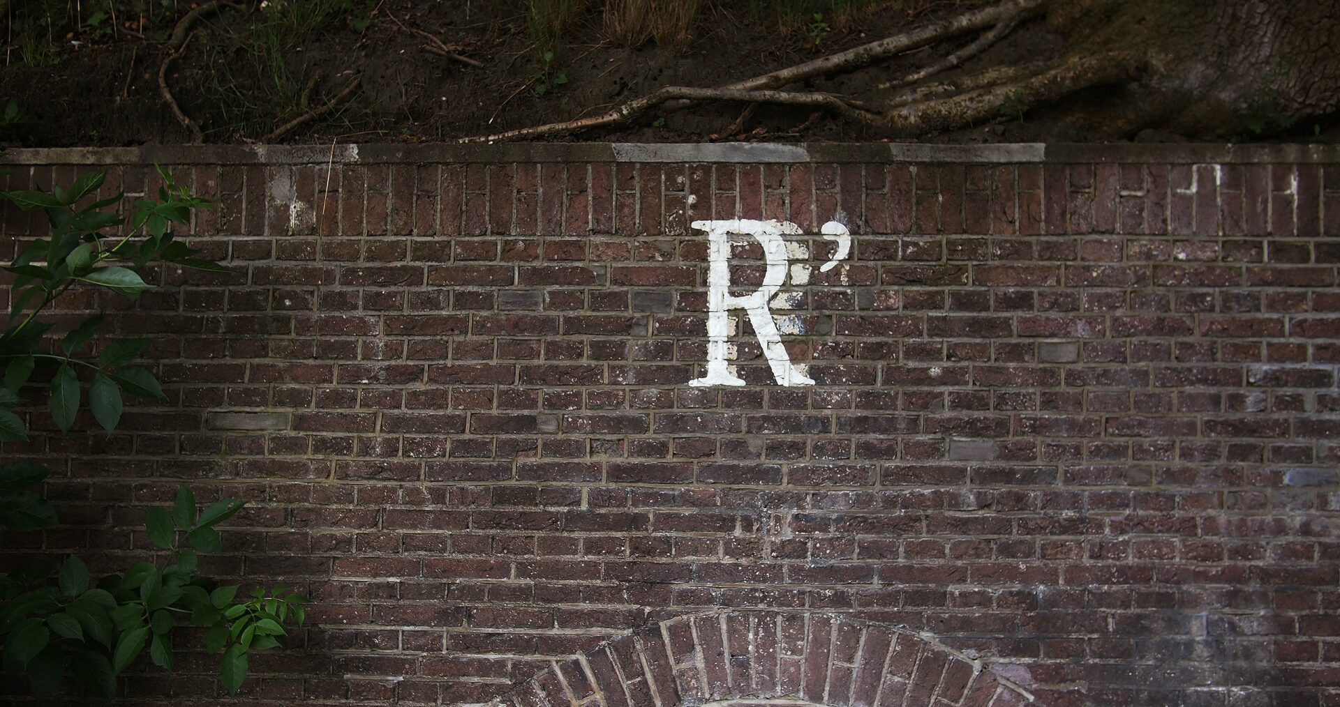 The capital letter R is painted in faded white paint on top of some dark, red bricks in an urban setting