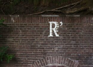 The capital letter R is painted in faded white paint on top of some dark, red bricks in an urban setting